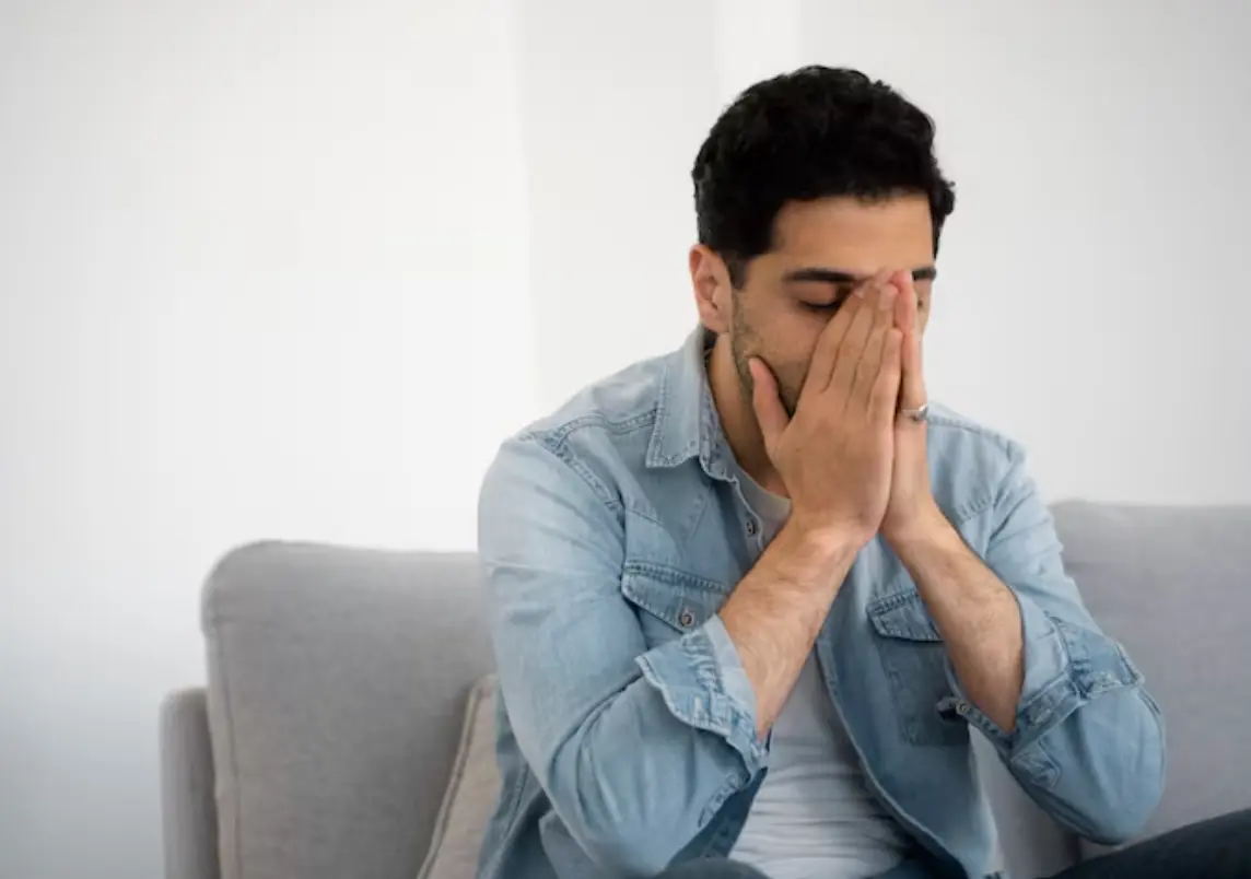 A man sitting on a sofa looking overwhelmed or deep in thought.