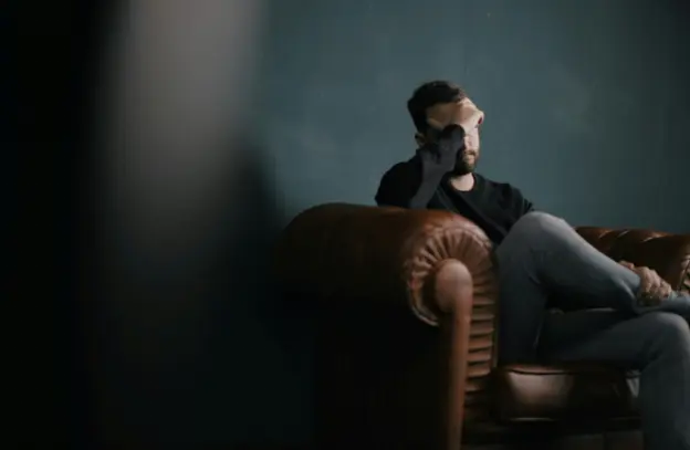 A man holding his head while sitting on a sofa