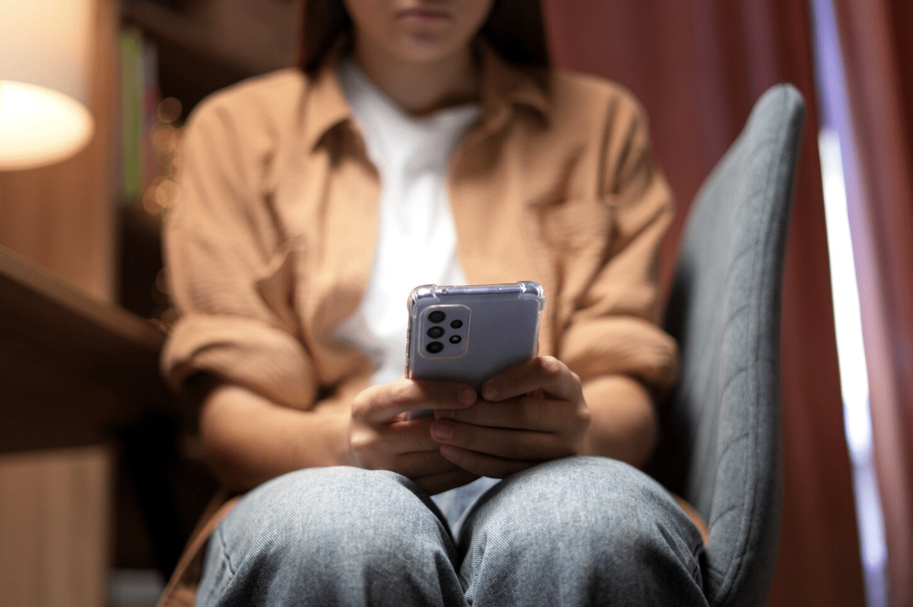 A woman looking distressed while holding her phone, suggesting a negative online interaction.