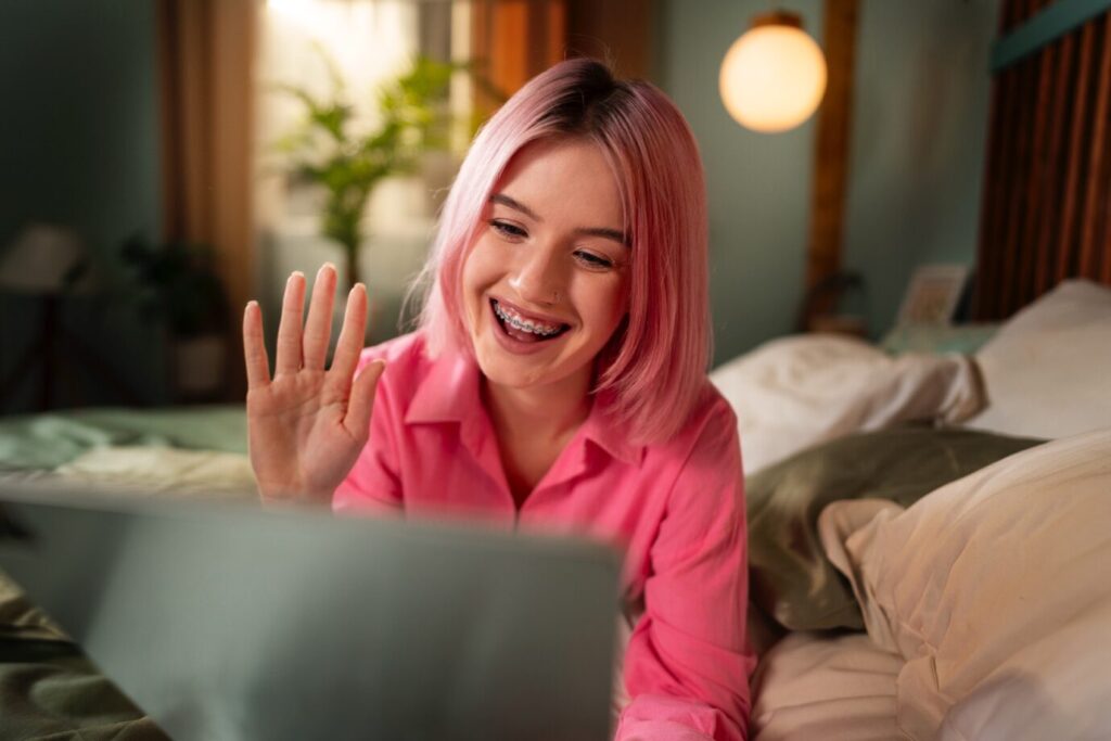 A smiling teenage girl in a pink shirt speaking to her therapist online.