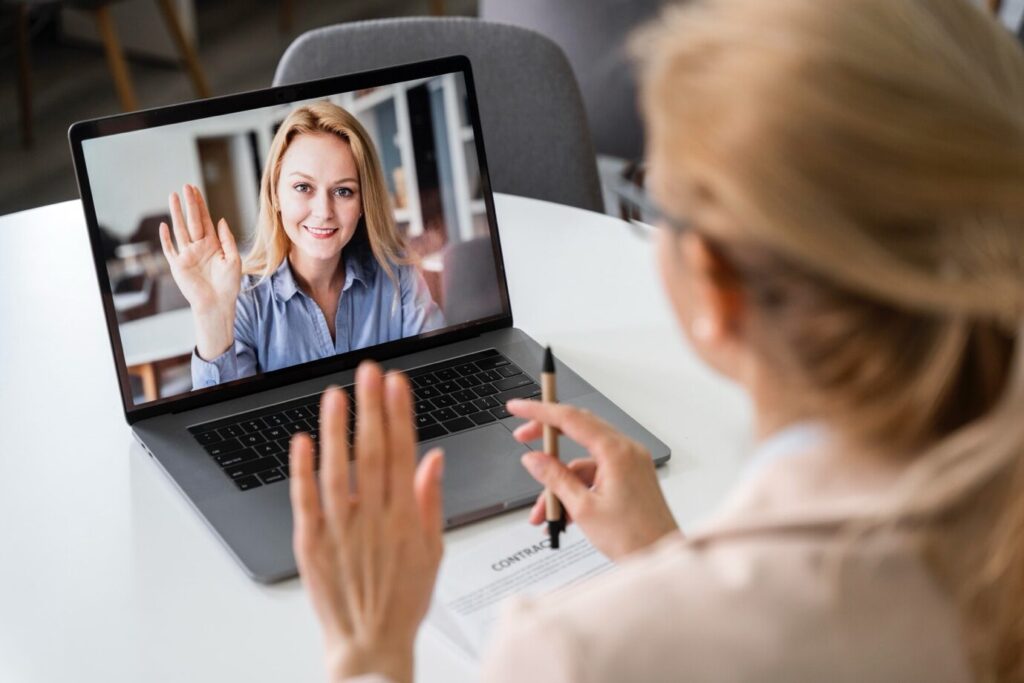 A woman speaking with a therapist via laptop in a cozy home setting.