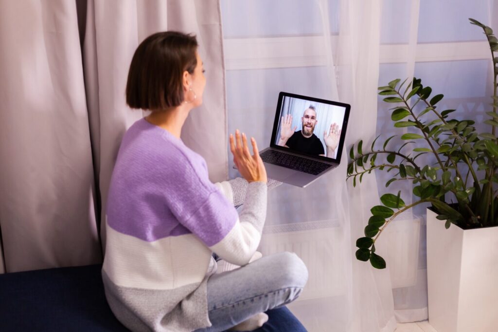 A therapist and patient smile and wave to each other through a secure video call.