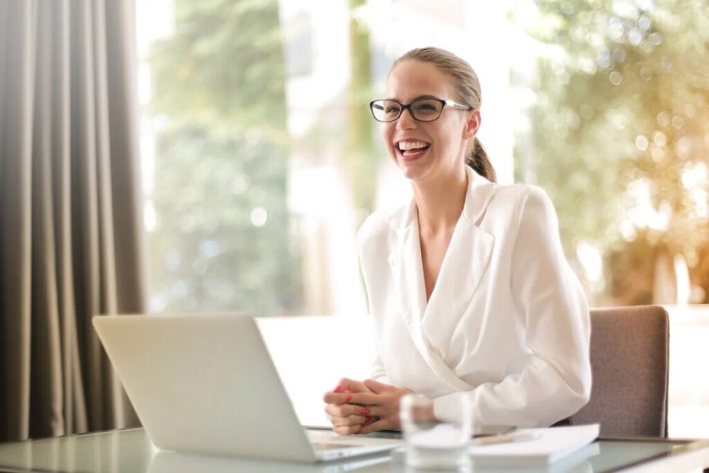 An image of a smiling woman sitting in front of her laptop at a table