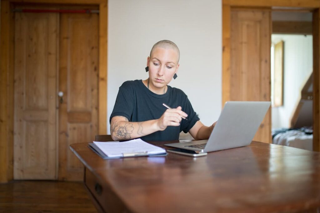 An image of a woman using her laptop while writing something on paper