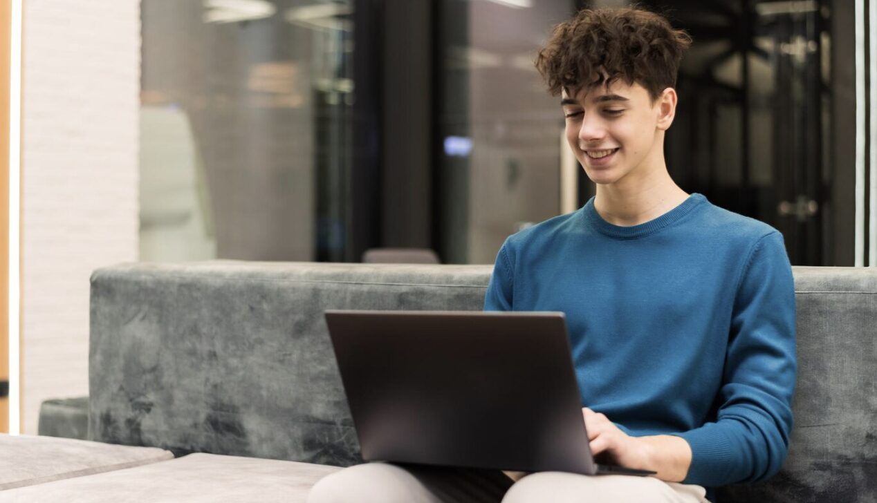 A smiling teenager engaged in an online therapy session via his laptop.